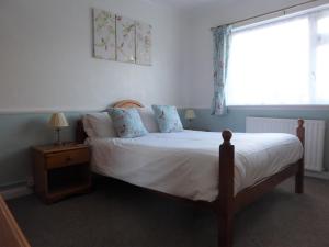 a bedroom with a bed with white sheets and a window at The Denewood in Sandown