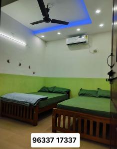 two beds in a room with a ceiling fan at Clap House Home in Guruvāyūr