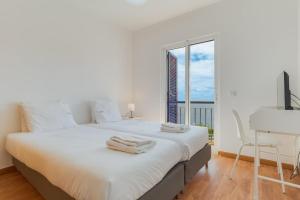 a white bedroom with a large white bed and a window at Esfera I Calm Stay With Parking & Workspace in Caniço