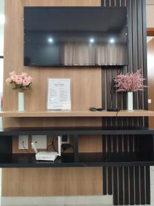 a tv on a wall with flowers on a shelf at Apartamento Moderno e Confortável in Lavras