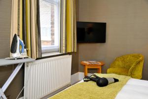 Habitación con cama, TV y silla. en Ardington Hotel, en Worthing