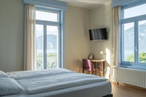 a bedroom with a bed and a desk and windows at Seminar-Hotel Rigi am See in Weggis