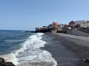 a beach with a black sand and water and buildings at La Cuevita, Playa de la Viuda in Candelaria
