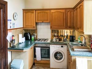 a kitchen with wooden cabinets and a washing machine at Gladstone Cottage in Castletown