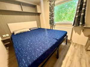 a bedroom with a blue bed in a room with a window at Chalet am Wattenmeer Holland in Lauwersoog