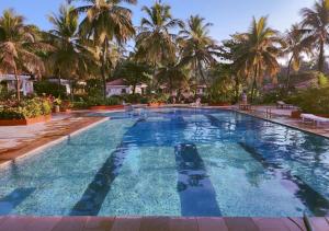 a large swimming pool with palm trees in the background at Beach villa South Goa in Arossim-Cansaulim