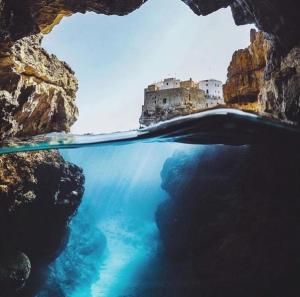 a cave in the water with a castle in the background at Wonderhouse in Polignano a Mare