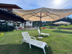 two white chairs and an umbrella in the grass at Albergo Scoiattolo Dolomites Experience in Falcade