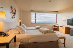 a bedroom with two beds and a desk and a window at Hotel Patagonico in Puerto Varas