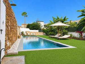 a swimming pool with green grass and an umbrella at Can Roig in Ses Salines