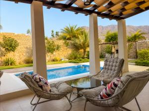 a patio with two chairs and a table and a swimming pool at Valley Farmhouse By Bait Zain in As Sīfah