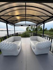two white couches sitting on a deck near the water at Kalna Raskumu Apartamenti in Vecpiebalga