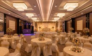 a banquet hall with white tables and chairs and a stage at Hotel Le Amritam in Dehradun