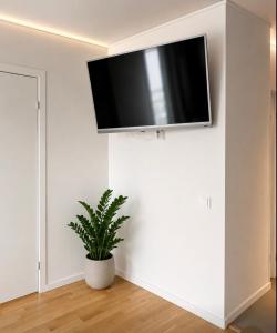 a flat screen tv on a white wall in a room with a plant at Nordic Central Apartment in Solna