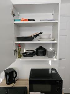 a kitchen shelf with pots and pans and a microwave at Modern Fully Contained En-Suite Room With Kitchen in Sidcup