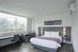 a hotel room with a bed and a desk and a window at Hotel bh El Poblado in Medellín