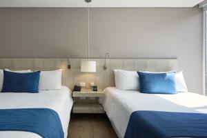 two beds in a hotel room with blue pillows at Hotel bh Bicentenario in Bogotá