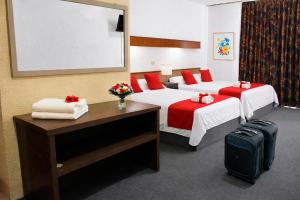 a hotel room with two beds with red pillows and a suitcase at HOTEL OASIS Matehuala in Matehuala +14 photos