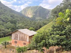 a barn in a field with mountains in the background at Recanto Salto Ano Bom in Corupá