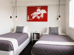 a bedroom with two beds and a painting on the wall at Bach By The Beach in Mount Maunganui