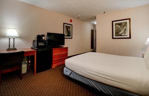 a hotel room with a bed and a desk with a television at Anchorage Inn & Suites - Portsmouth in Portsmouth