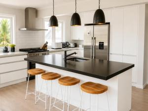 a kitchen with a black counter top and wooden stools at Bach By The Beach in Mount Maunganui