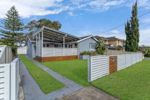 a home with a white fence and grass at Blue Summer House in Long Jetty