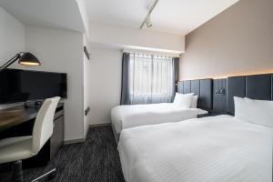 two beds in a hotel room with a desk and a tv at Hotel Vista Sapporo Odori in Sapporo