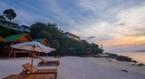 a beach with two benches and an umbrella on the sand at The Green Hotel in Ko Lipe