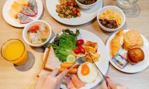 a table with plates of breakfast foods and a person with a fork and knife at Diya Hotel Bangkok in Amphoe Phra Khanong