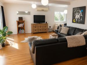 a living room with a black couch and a flat screen tv at Bach By The Beach in Mount Maunganui