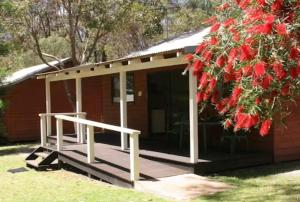 a cabin with a porch and a tree with red flowers at Discovery Parks Margaret River in Cowaramup