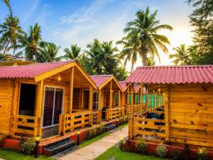 a row of wooden cottages with palm trees in the background at Village Sunset Paradise Beach Resort in Morjim