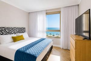 a bedroom with a bed and a television and a window at מגדל אלמוג חיפה - דירות "בלו ביץ'" על הים in Haifa