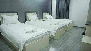 two beds in a room with white sheets at Hotel City Land Tashkent in Yakkasaray