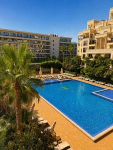 a swimming pool with chairs and a palm tree and buildings at ЛУКСОЗЕН АПАРТАМЕНТ В 4 звезден хотел in Golden Sands