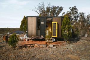 a tiny house with a yellow door in a field at Raya and Aiden Farm House by Tiny Away in Cooma