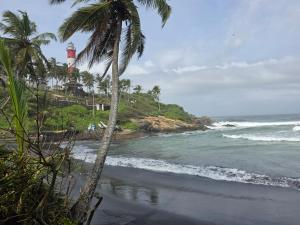 a beach with a lighthouse and palm trees and the ocean at SITER Holidays Villa in Kovalam