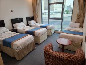 a room with three beds and a chair and a window at Qimmat AlAwali Hotel in Az Zahrāʼ