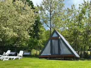 a black triangular house with two white chairs and trees at STORY GLAMPING POLOVRAGI in Racoviţa