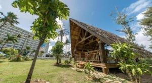 a thatch roofed house with a palm tree and a building at Saipan World Resort in Susupe