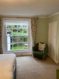a bedroom with a green chair and a window at Stratton Gardens in Bude