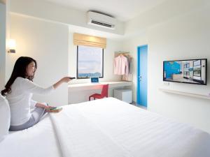 Hop Inn Buriram في بوريرام: امرأة تجلس على سرير في غرفة فندق