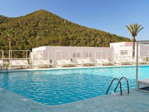 a swimming pool with chairs and a mountain in the background at Mondrian Beach Lifestyle Resort By Accor in Cala Llonga
