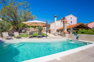 a swimming pool with an umbrella and chairs and a house at Villa Loznati in Cres
