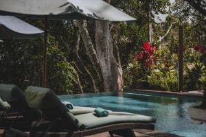 a swimming pool with two chairs and an umbrella at The Hidden Paradise Ubud - CHSE Certified in Ubud