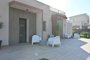 a patio with white chairs in front of a building at Kleos Luxury Rooms in Porto Empedocle