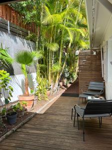 a wooden deck with chairs and palm trees on it at Bungalow Tec-Tec Proche plage et centre Saint Leu in Saint-Leu