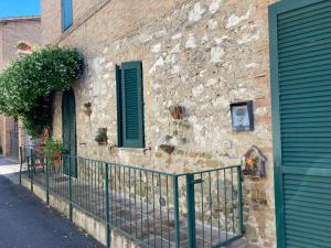 a stone building with green shutters and a fence at La Tua Casina in Torrenieri