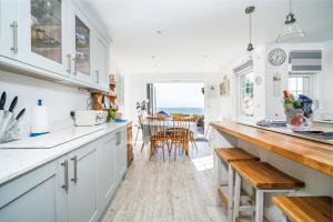 a kitchen with white cabinets and a dining room with the ocean at Jan Dee Cottage in Ventnor